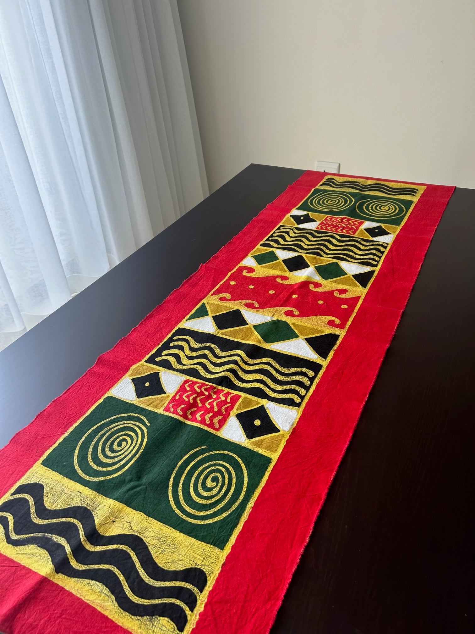 African batik table cloth with vibrant geometric and symbolic patterns on high-quality cotton fabric, displayed on a dark table.