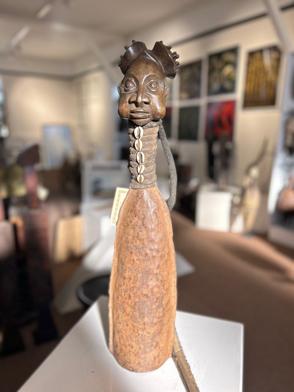 Bamum tribe bronze bell with leather handle and cowrie shell embellishments, symbolizing royalty and cultural significance, displayed in Rogl Souvenirs & Gallery.