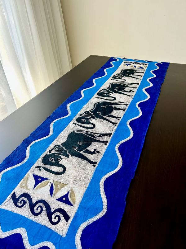 Batik style table cloth featuring a herd of elephants in vibrant colors, crafted from high-quality cotton fabric, displayed on a dark wooden table.