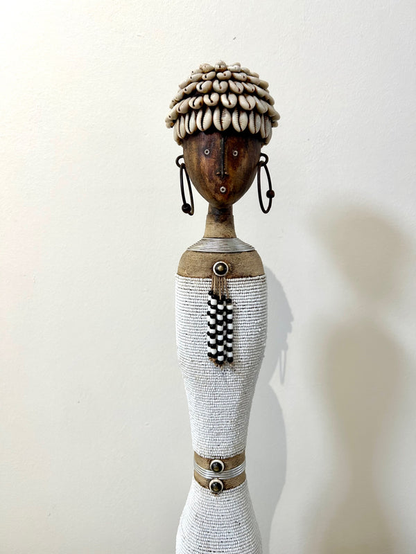 Beaded Namji doll from Cameroon with cowrie shell headdress and white attire, representing fertility and motherhood, available at Rogl Souvenirs & Gallery.
