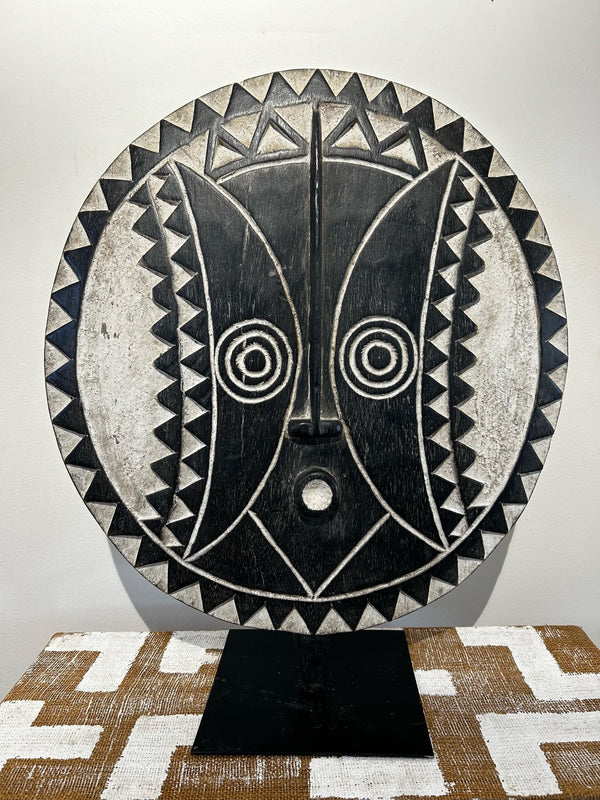 African Bobo tribe sun mask from Burkina Faso, black and white, round with prominent features, used in ceremonies for harvest celebrations and ancestral worship, displayed at Rogl Souvenirs & Gallery.