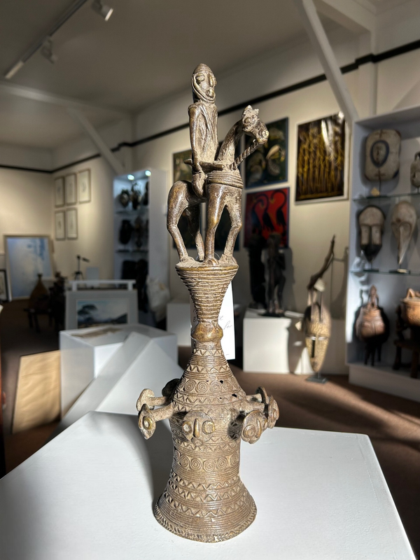 Bronze Yoruba tribal bell sculpture, symbolizing authority and cultural heritage, displayed in an art gallery setting.