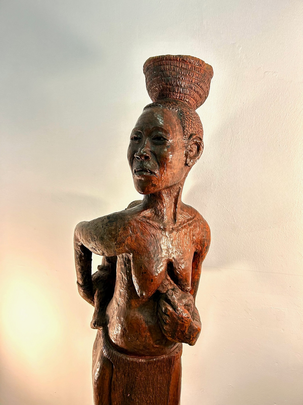 Wood sculpture of a Bushman woman from Namibia, titled "A Mother's Embrace," depicting a mother with a child on her back and a basket on her head, crafted from heavy ironwood.
