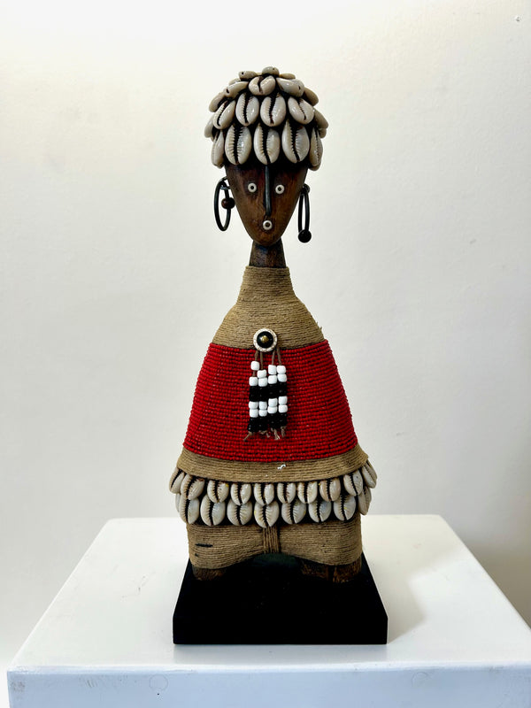 Beaded Namji doll from Cameroon, adorned with cowrie shells and red beads, representing fertility and motherhood, displayed at Rogl Souvenirs & Gallery.