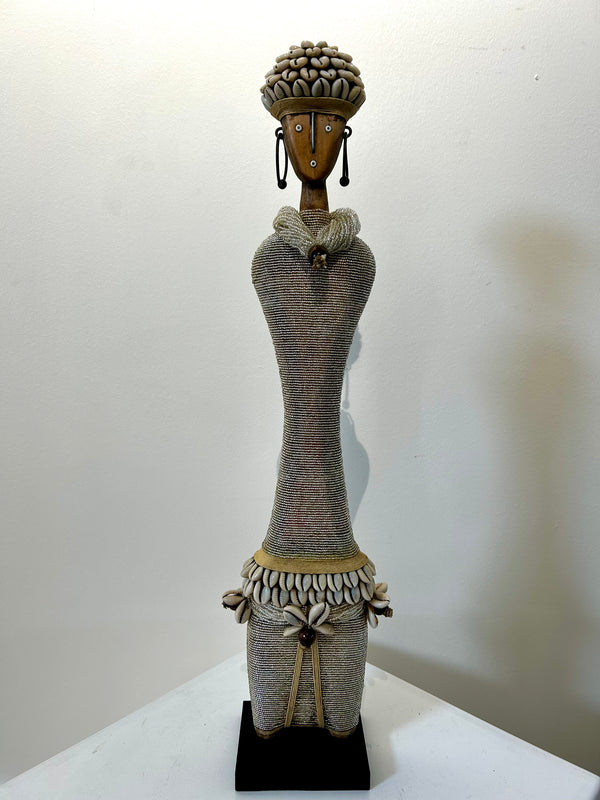 Beaded Namji doll sculpture from Cameroon, adorned with silver beads and cowrie shells, representing fertility and motherhood, displayed at Rogl Souvenirs & Gallery.
