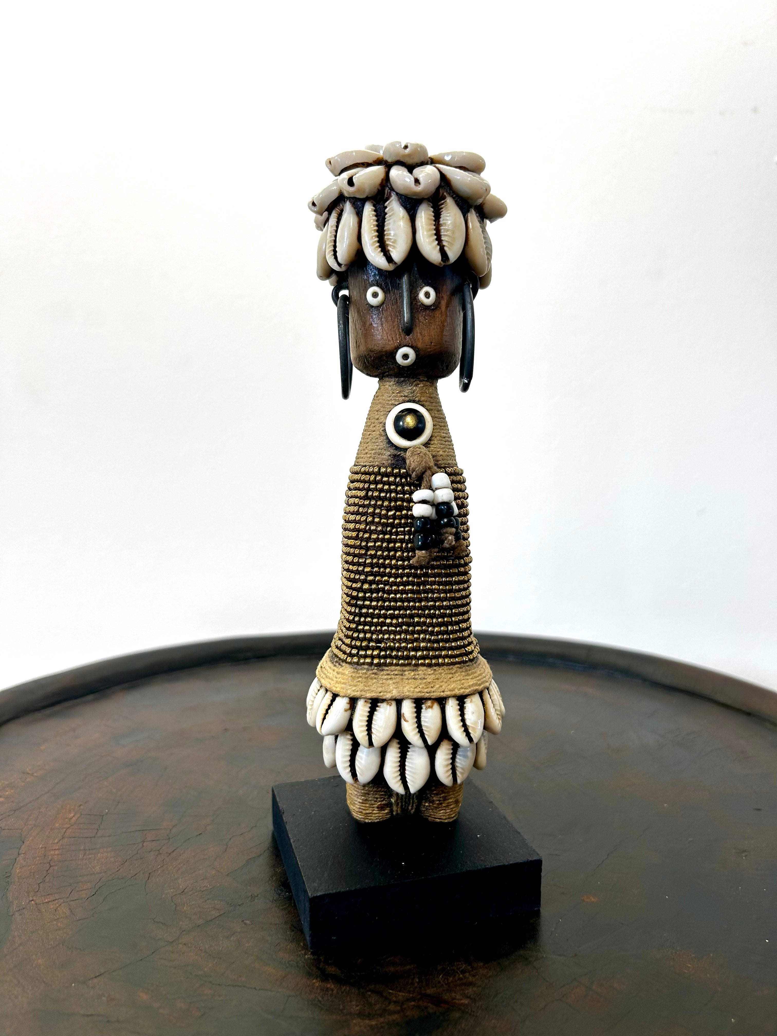 Gold Namji doll sculpture from Cameroon adorned with beads and cowrie shells, representing fertility and motherhood.