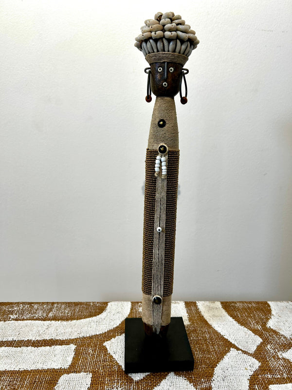 Namji doll sculpture from Cameroon, adorned with beads and cowrie shells, representing fertility and motherhood, displayed at Rogl Souvenirs & Gallery.