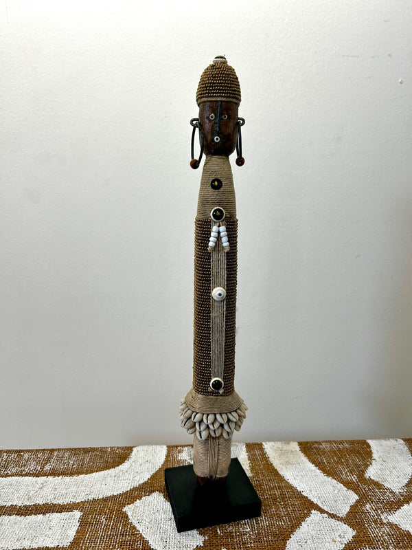 Gold Namji doll sculpture from Cameroon, adorned with beads and cowrie shells, representing fertility and motherhood, displayed at Rogl Souvenirs & Gallery.