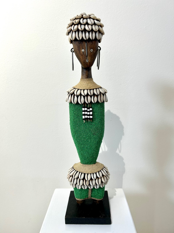Namji doll sculpture from Cameroon, adorned with green beads and cowrie shells, representing fertility and motherhood.