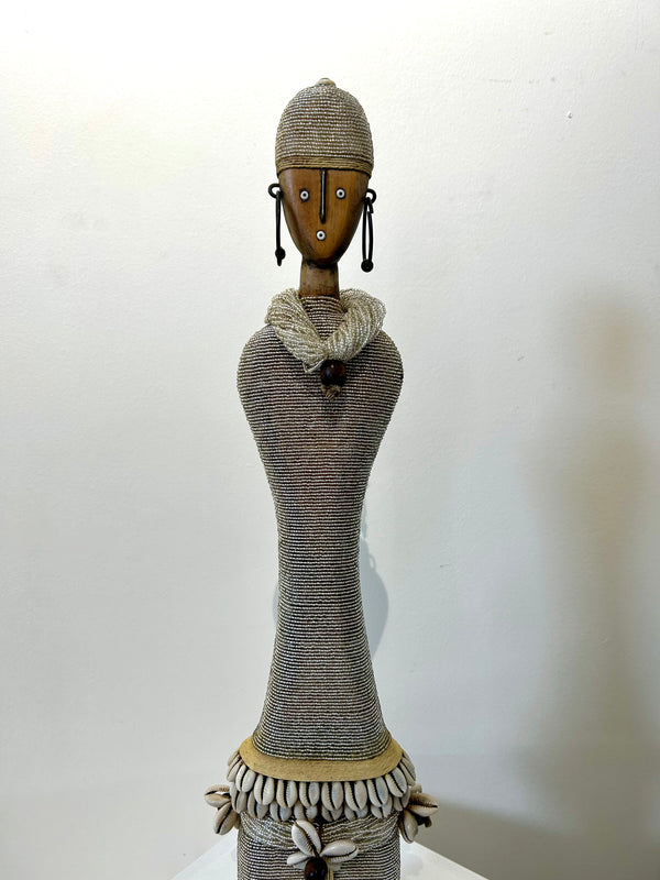 Silver Namji doll sculpture from Cameroon adorned with beads and cowrie shells, representing fertility and motherhood.