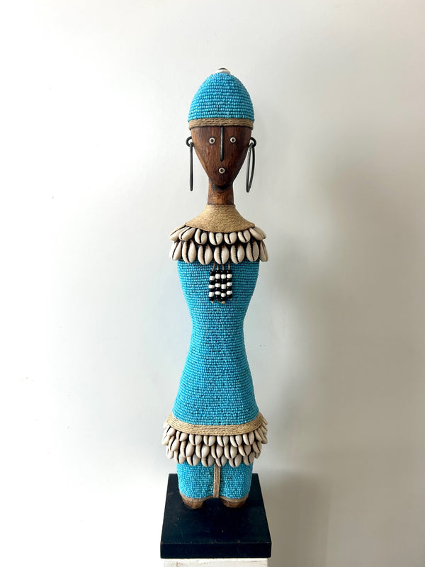 Turquoise Namji doll sculpture from Cameroon adorned with beads and cowrie shells, representing fertility and motherhood.