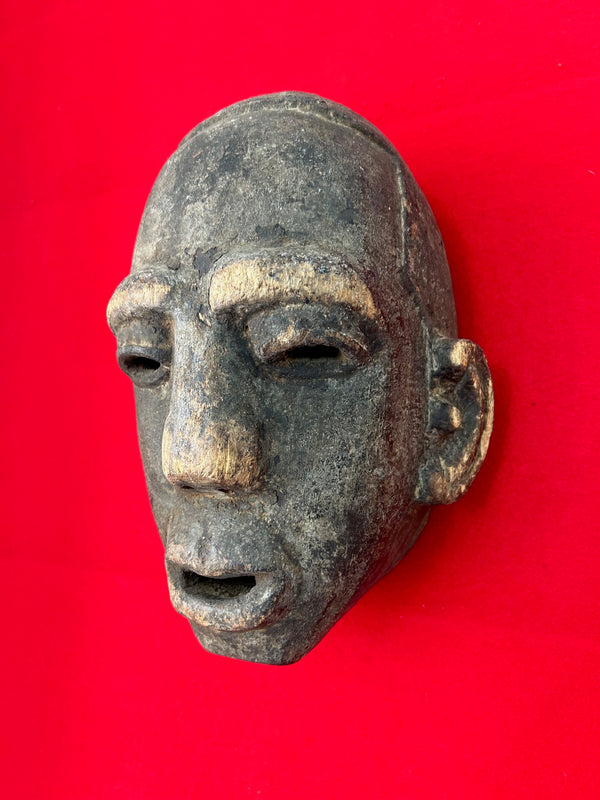 Mbona tribe night mask from Congo-Zaire with captivating patina, handcrafted from heavy wood, displayed on a vibrant red background.