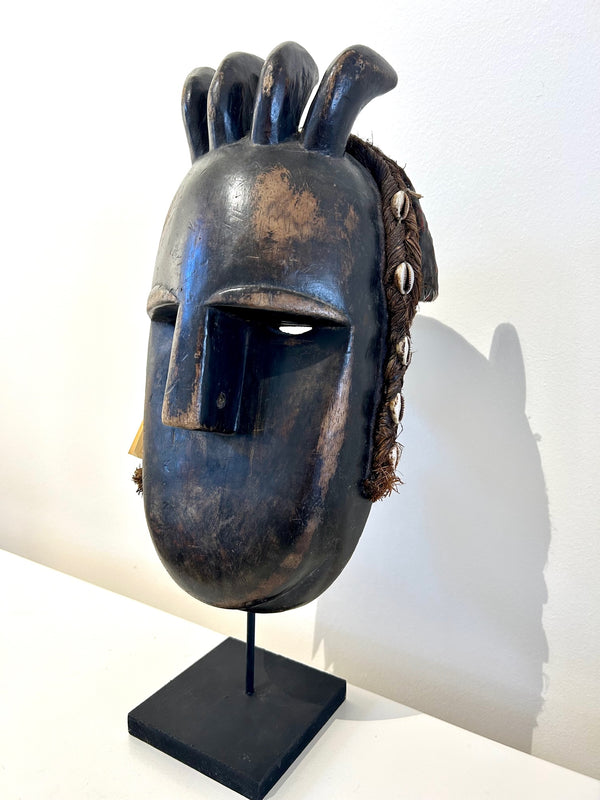 Dan tribe mask from Ivory Coast with dark wood, cowrie shells, and braided palm leaves, showcasing cultural craftsmanship and patina.