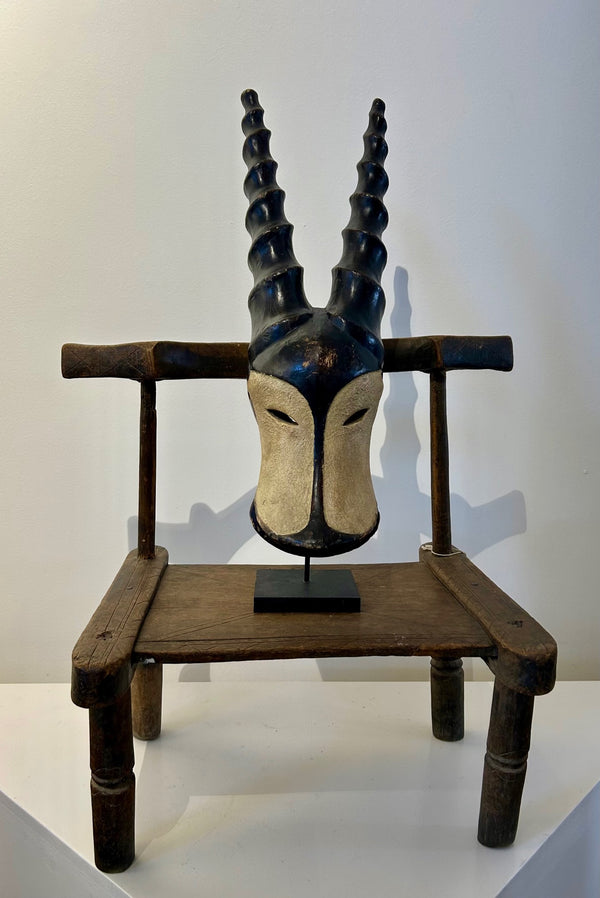 Duala antelope mask with black and white contrasts, featuring intricately carved horns symbolizing power and fertility, displayed on a wooden stand.