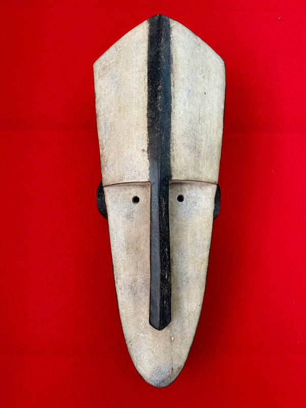 Classic Fang mask from Gabon with geometric design, white and black colors, used in ceremonies, displayed on a red background.
