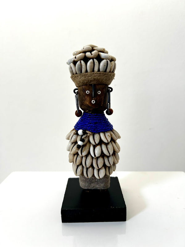 Indigo beaded Namji doll from Cameroon adorned with cowrie shells, representing fertility and motherhood, displayed at Rogl Souvenirs & Gallery.