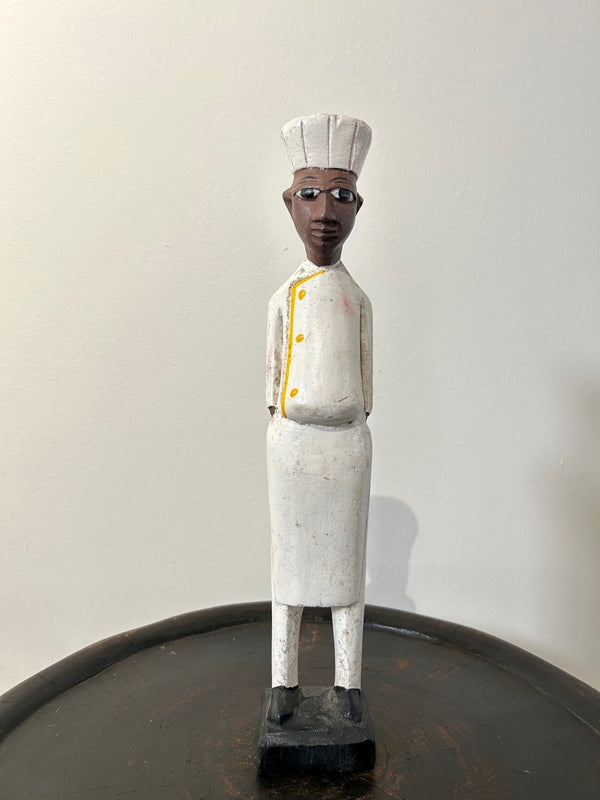 Wooden colonial figure sculpture from Ivory Coast depicting a chef, hand-carved with intricate details, wearing a white uniform and hat, symbolizing historical colonial influences in West Africa.
