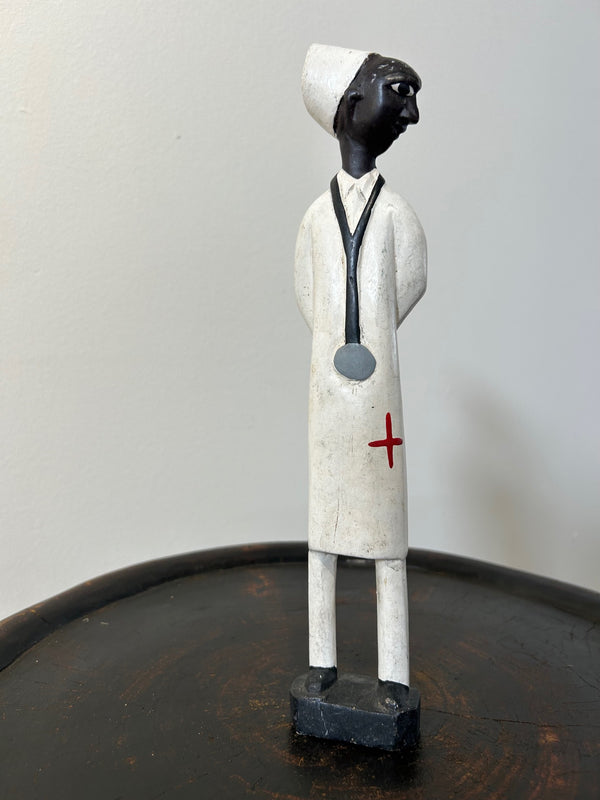 Wooden colonial figure sculpture of a doctor from Ivory Coast, hand-carved with a stethoscope and white coat, symbolizing historical colonial influence, available at Rogl Souvenirs & Gallery.
