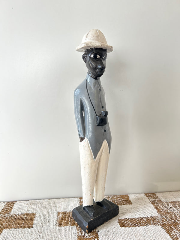 Wooden colonial figure sculpture from Ivory Coast, hand-carved, depicting a historical colonial figure with a camera, multi-colored, displayed on a patterned surface.