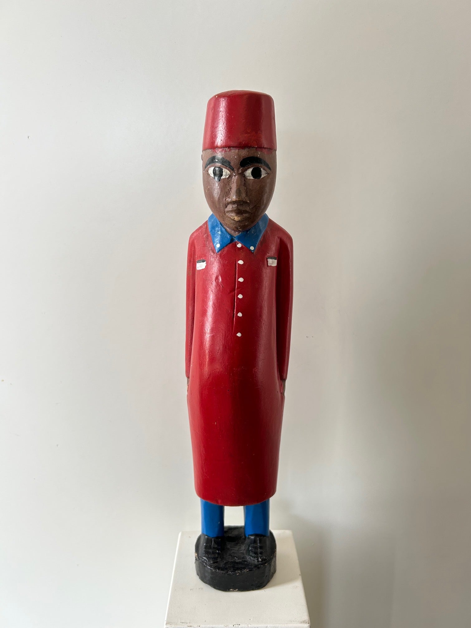 Wooden colonial figure sculpture from Ivory Coast, hand-carved, depicting a historical colonial messenger in red attire with blue accents, displayed at Rogl Souvenirs & Gallery, African art gallery.