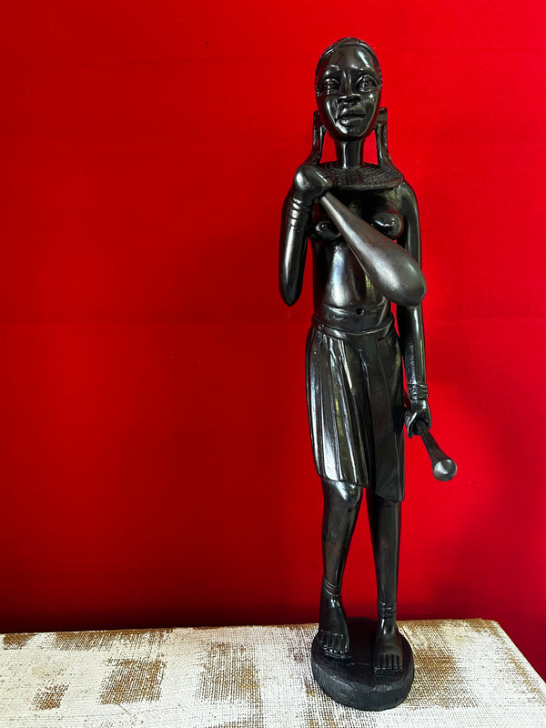 Maasai woman sculpture in traditional attire, carved from ebony wood, displayed against a red background at Rogl Souvenirs & Gallery, African art gallery.