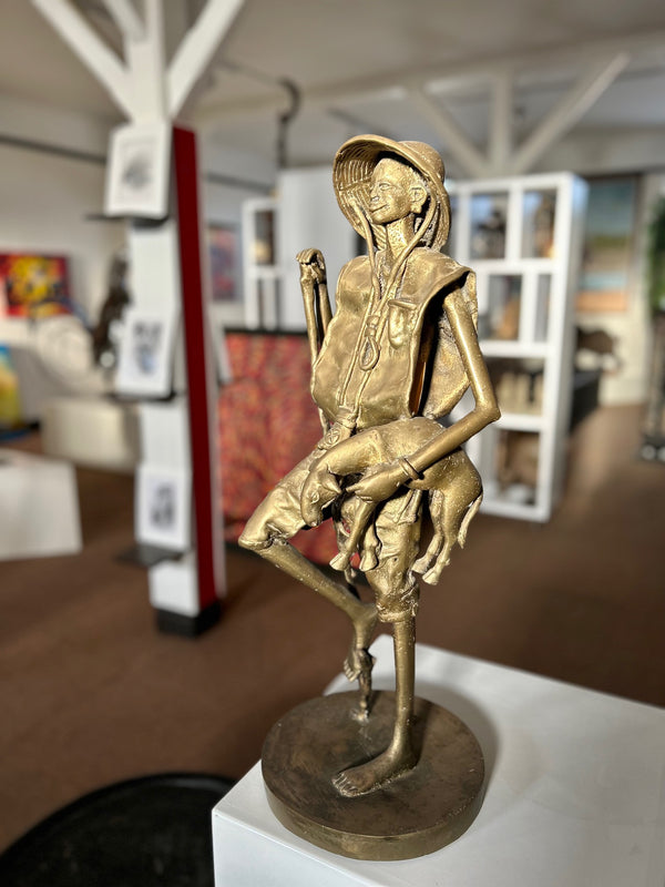 Bronze sculpture of a Mossi tribe shepherd cradling a lamb, showcasing intricate textures and cultural heritage at Rogl Souvenirs & Gallery.