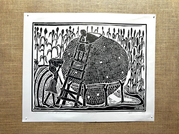 Black and white woodcut print of Namibian villagers filling a traditional grain storage basket with mahango, showcasing cultural heritage and agricultural practices.