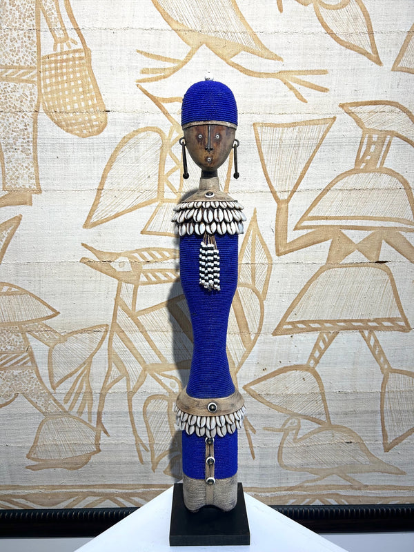 Beaded Namji doll in indigo with cowrie shells, representing fertility and motherhood, from the Namji tribe in Cameroon, displayed at Rogl Souvenirs & Gallery.