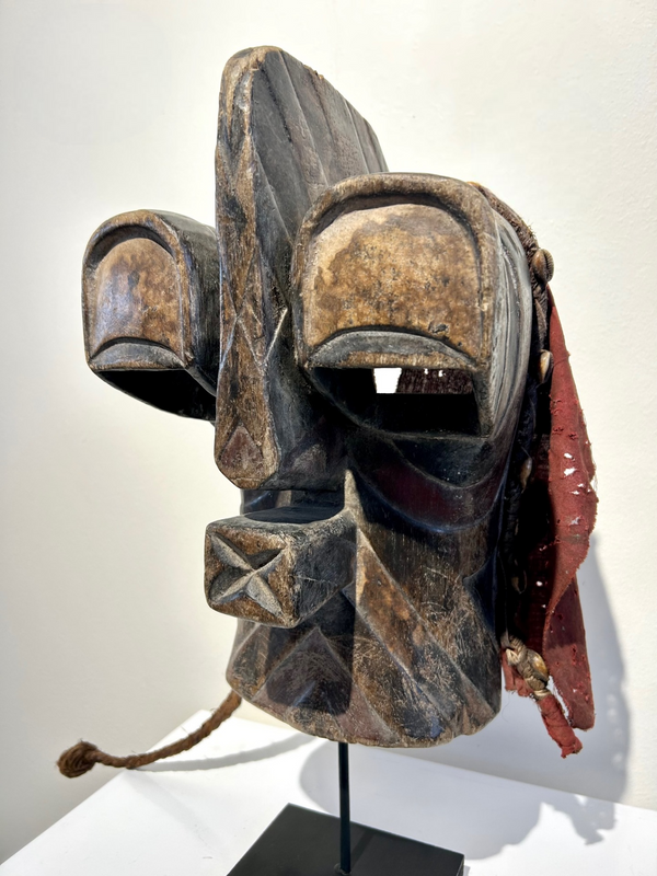 abstract Songye-Basonge wood mask from Congo-Zaire with large eyes and nose, decorated with cowrie shells and braided palm leaves, displayed at Rogl Souvenirs & Gallery
