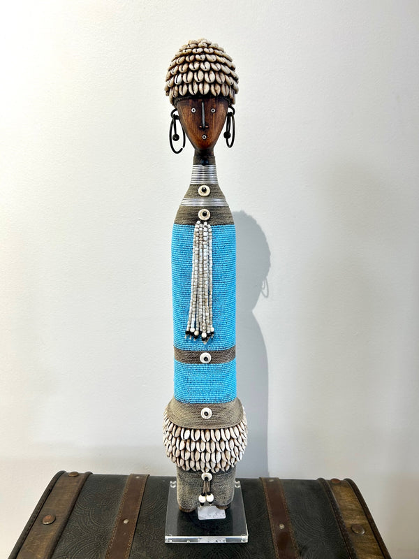 Turquoise beaded Namji doll from Cameroon adorned with cowrie shells, representing fertility and motherhood, displayed at Rogl Souvenirs & Gallery.