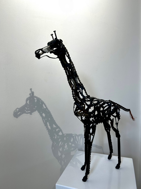 Giraffe sculpture made from upcycled metals, showcasing intricate details and lifelike presence, displayed in an art gallery setting.