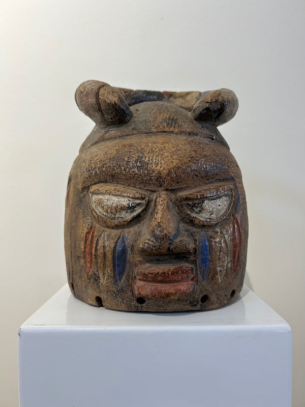 Yoruba helmet mask from Nigeria, intricately carved from heavy wood, featuring multi-color detailing, used in tribal ceremonies, displayed at Rogl Souvenirs & Gallery.